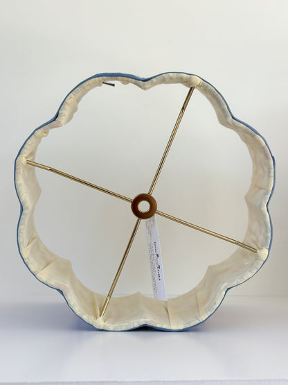 A scalloped flower-shaped fabric lampshade with a cream-colored inner lining, a blue outer edge, and gold-toned metal support rods, shown on a white surface against a white background.